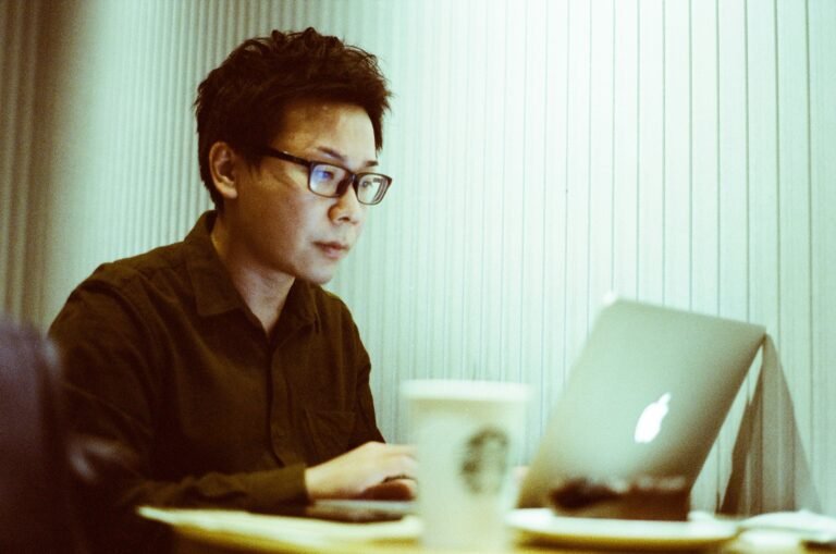 Asian man seated at a table working on a laptop, representing a fleet owner using a commercial vehicle loan and interest calculator