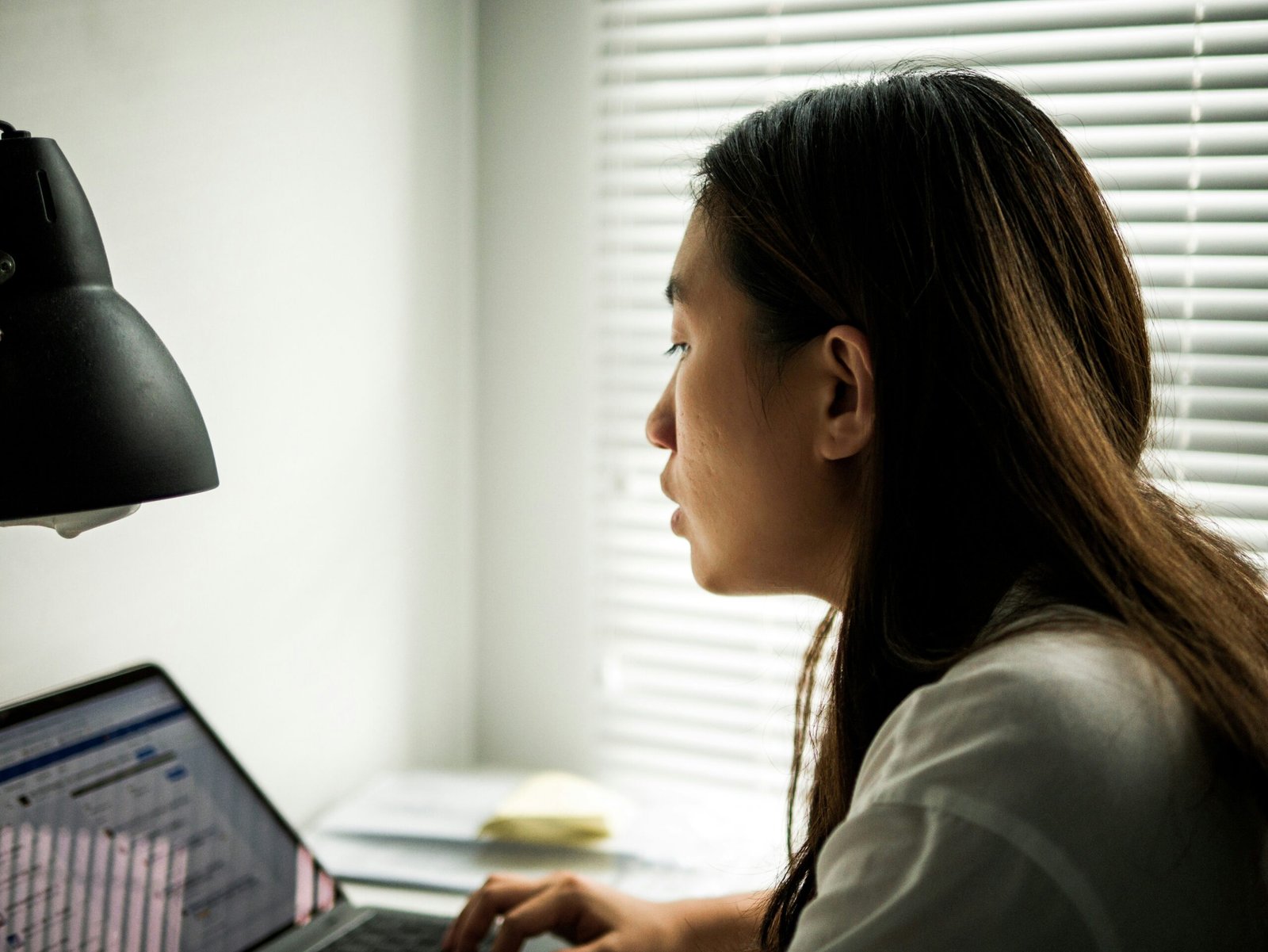 Asian professional in an office reviewing figures on a laptop, calculating total cost of ownership for a commercial vehicle
