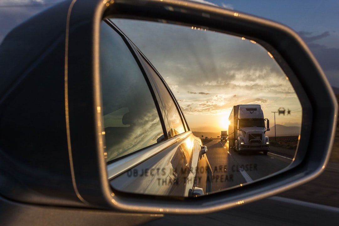 Reflection of a freight truck in a vehicle's side mirror at sunset, illustrating heavy vehicle blind spot safety for Singapore fleet drivers