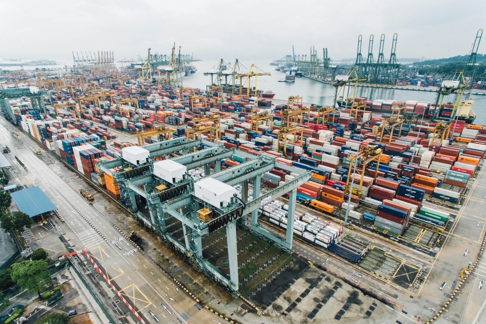 Busy cargo port with container ships and trucks, representing the commercial fleet operations that require vehicle financing in Singapore